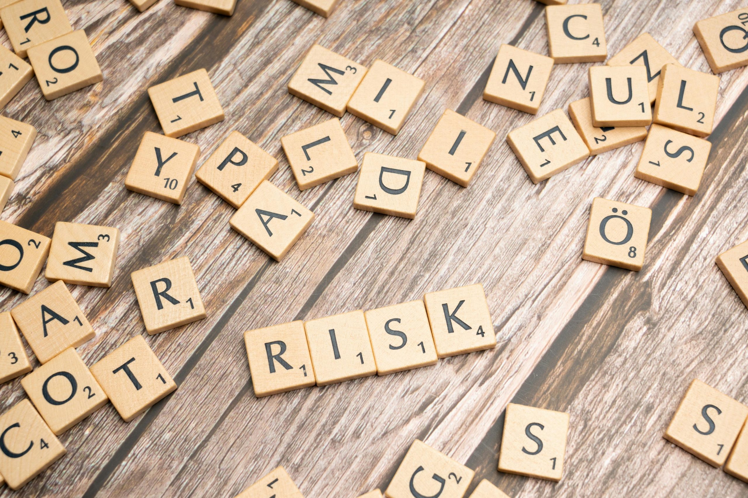 Wooden letter tiles scattered on a rustic wood surface, with four tiles arranged to spell the word RISK.