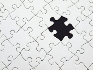 Close-up of a white jigsaw puzzle with one missing piece, revealing a dark empty gap underneath.