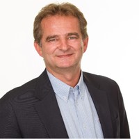Smiling middle-aged man wearing a dark blazer over a light button-up shirt, posed against a plain white background
